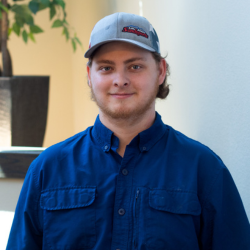 Alex Edwards, Plant Operations Director at Cedar Ridge Village, smiling in a blue shirt and cap, standing against a neutral background with greenery.