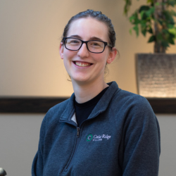 Amber Eivins, Culinary Director at Cedar Ridge Village, smiling in a gray sweatshirt with the Cedar Ridge logo, set against a softly lit background.