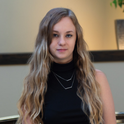 Stevie Sargent, AL Director at Cedar Ridge Village, portrait with long wavy hair and black top, indoor setting.